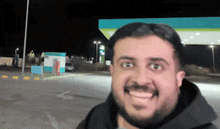 a man with a beard is smiling in front of a petrol station