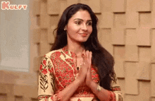 a woman with long hair is standing in front of a wall with her hands folded in prayer .