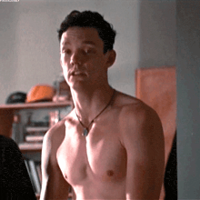 a shirtless man with a necklace around his neck is looking at the camera