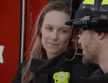 a man and a woman are standing next to each other and the man is wearing a helmet with a yellow stripe on it