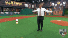 a man in a white shirt and tie is standing on a baseball field with a mlb logo