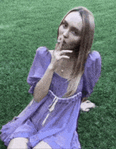 a woman in a purple dress is smoking a cigarette while sitting on the grass .