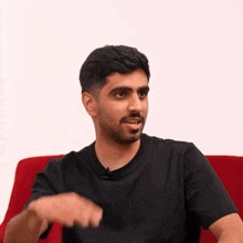 a man in a black shirt is sitting on a red couch with his hand out