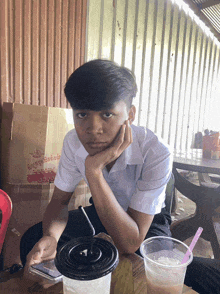 a young boy sits at a table with a cup of drink and a cardboard box that says ' a ' on it