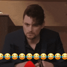 a man in a suit is sitting at a table with a row of laughing emojis behind him