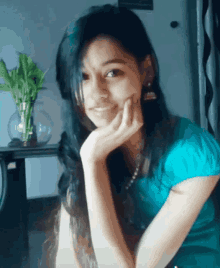 a woman in a blue shirt is smiling with her hand on her face
