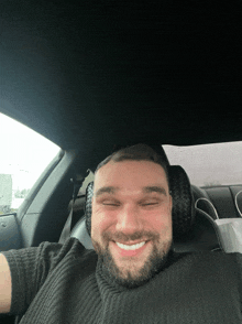 a man with a beard is smiling in a car with his eyes closed