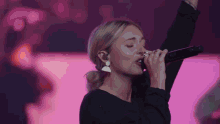 a woman is singing into a microphone with her arms in the air