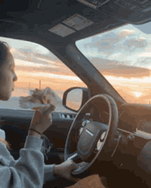 a woman is driving a range rover while eating a sandwich
