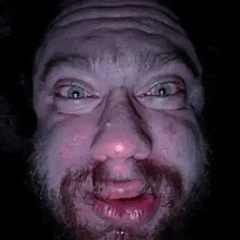 a close up of a man with a beard making a funny face in the dark .