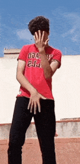 a young man in a red shirt is covering his face with his hands while standing on a rooftop .
