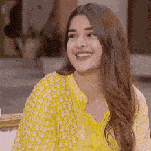 a woman in a yellow dress is smiling and looking at the camera .