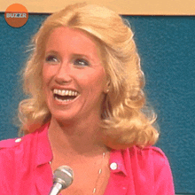 a woman in a pink shirt is smiling in front of a microphone with a buzzr logo in the background