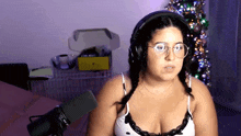 a woman wearing headphones and glasses stands in front of a microphone with a christmas tree in the background