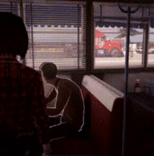 a man is sitting in a booth in a diner looking out a window