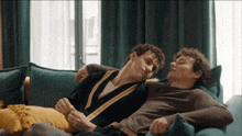 two men are laying on a blue couch and hugging each other