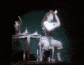 a woman is sitting on a stool on a stage in front of a table and mirror .