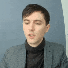 a young man wearing a suit and turtleneck is making a funny face .