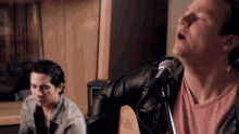 a man singing into a microphone with another man playing a guitar behind him