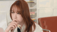 a young woman with red hair is sitting at a table with her hand on her chin .