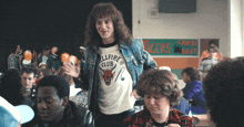 a man wearing an allfire club t-shirt stands in a crowded room