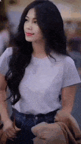 a woman with long black hair wearing a white t-shirt and blue jeans is walking down the street .