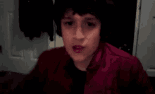a young boy in a red jacket is making a funny face while looking at the camera .