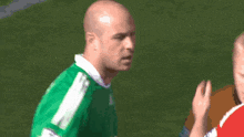 a bald man wearing a green adidas jersey stands on a field
