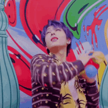 a young man with purple hair is standing in front of a colorful wall holding a blue balloon .