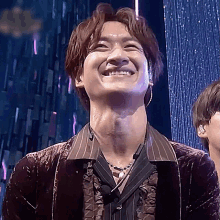 a man wearing a striped shirt and a pearl necklace is smiling on a stage