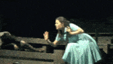 a woman in a blue dress is sitting on a fence talking to another woman