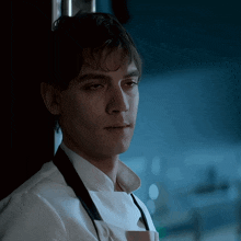 a man wearing an apron and a white shirt looks at something
