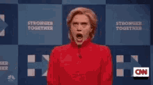 a woman in a red shirt is screaming in front of a sign that says " stronger together "