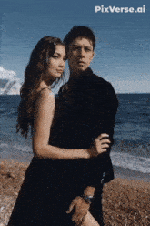 a woman in a black dress is hugging a man in a black suit on the beach