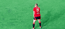 a female soccer player wearing a red jersey with the number 19 on it is standing on a green field .