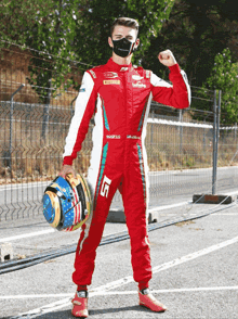 a man in a red and white sparco suit holds a blue helmet