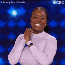 a woman stands in front of a microphone with her hands folded in front of her face and the words family feud canada behind her