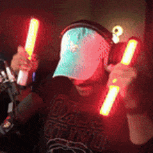 a man wearing a hat and headphones is holding glowing sticks in his hands .