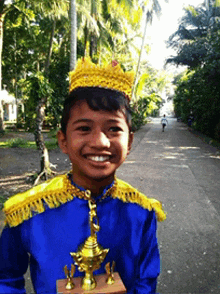 a young boy wearing a crown is holding a trophy and smiling