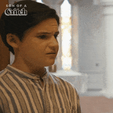 a young man in a striped shirt stands in front of a stained glass window with the words son of a critch above him