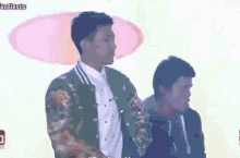 a man in a green jacket is standing next to another man in a white shirt .