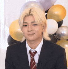 a young man in a suit and tie is standing in front of balloons