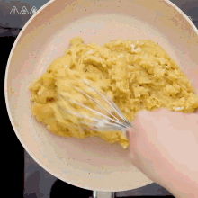 a person is whisking something in a pan with a warning sign above it