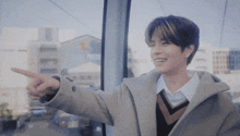 a young man wearing a coat and a sweater is pointing