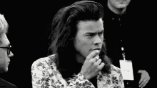 harry styles is wearing a floral jacket and smoking a cigarette .