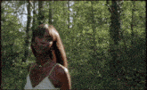 a woman in a white dress stands in a forest