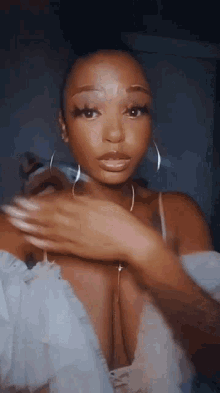 a woman wearing a white top and hoop earrings looks at the camera