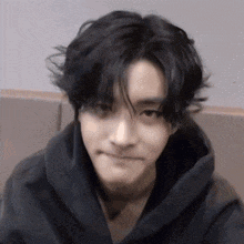 a young man with black hair is wearing a black hoodie and making a face .
