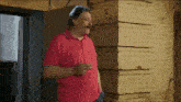 a man in a red polo shirt stands in front of a yellow brick wall