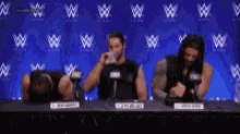 three wrestlers are sitting at a table drinking water